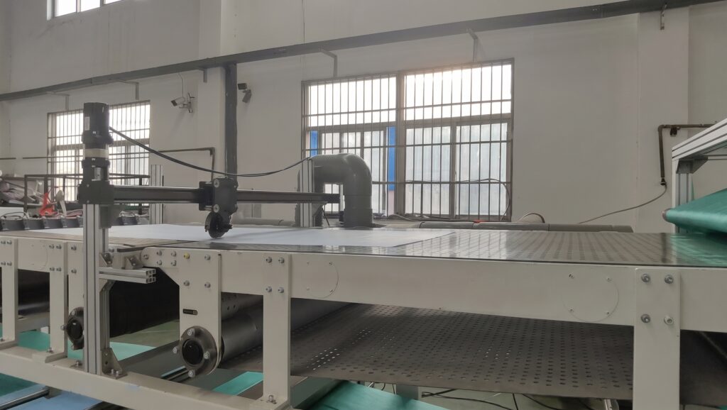 Automated medical drape and bedsheet manufacturing machine with conveyor belt and cutting system in a factory.