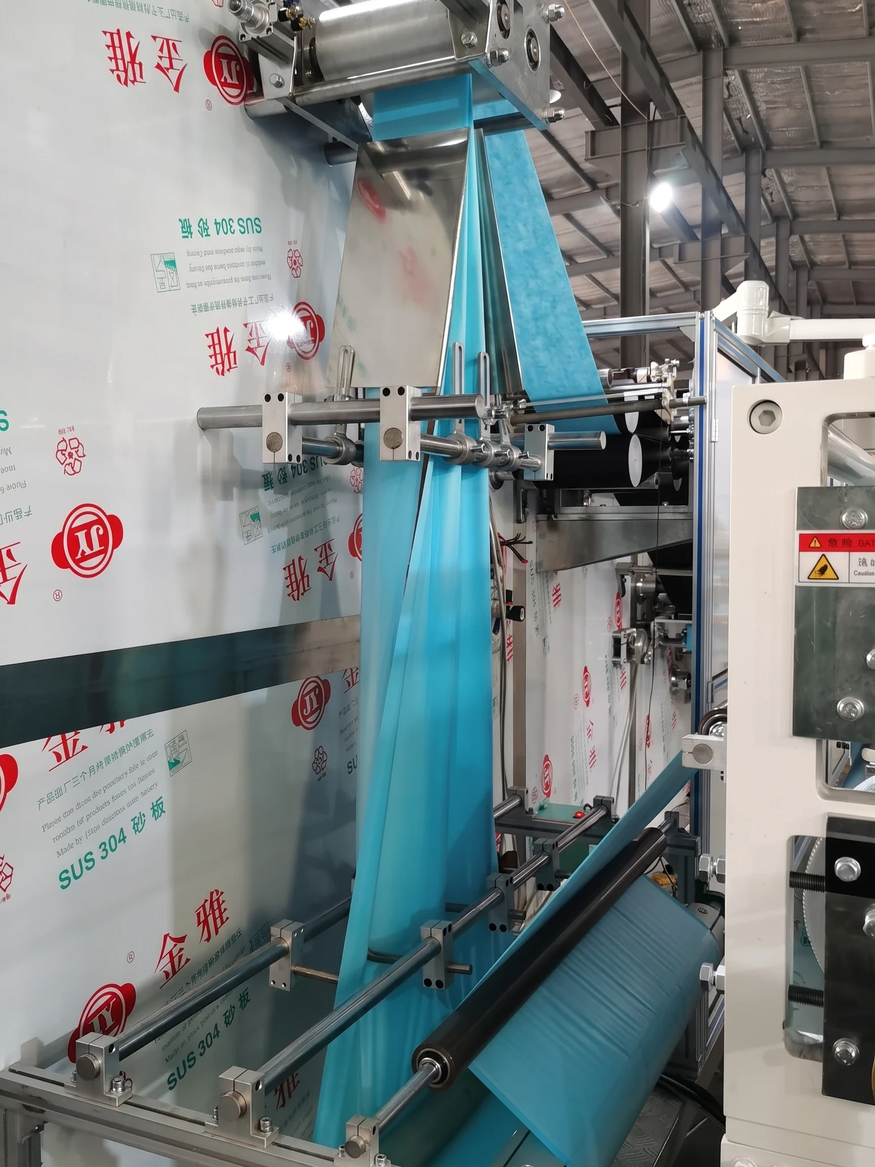 Industrial non-woven fabric fan-folding machine section processing light blue material with automated guides and stainless steel panels