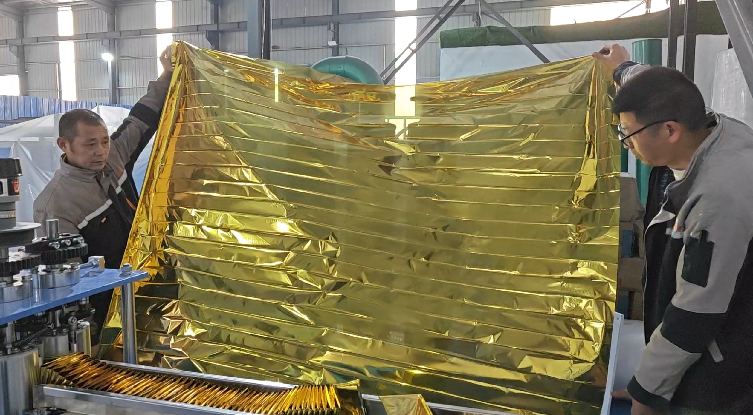 Workers inspecting a finished emergency blanket folded by the ZXJ emergency blanket folding machine during quality check.